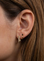 Close-up of a woman's ear adorned with two piercings: a small 18k gold plated hoop with a black stone and a larger Pavé Gold Hoop featuring sparkling CZ stones, framed by brown hair.