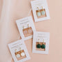 The JaxKelly Gemstone Mini Drop collection includes Rose Quartz (pink, love), Amazonite (green-blue, hope), Mother of Pearl (white, calming), and Malachite (green, growth) earrings—all elegant, gold plated, and tarnish-free.