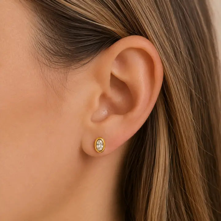 A JaxKelly Oval Bezel - White CZ stud earring worn in an earlobe.