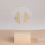 JaxKelly Sunburst Studs, crafted in gold vermeil and adorned with pavé stones, are showcased on a clear acrylic stand with a light wooden base against a neutral background.