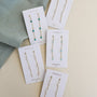 Five pairs of JaxKelly Gemstone Chain Drop - Amazonite earrings with 18k gold plating are displayed on branded cards, featuring Amazonite, turquoise, rose quartz, and opal next to a folded green cloth.