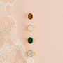 Four JaxKelly 18k gold plated rings, including the Malachite Signet Ring, each with unique stones, are arranged vertically on a light peach background next to white lace fabric.