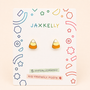 Candy Corn Enamel Flat Back Kids Earrings by JaxKelly displayed on a white card with colorful geometric designs. The card features the JaxKelly brand, highlights their hypoallergenic and kid-friendly posts. These adorable earrings for kids showcase yellow, orange, and white enamel sections—perfect hypoallergenic earrings for sensitive ears.