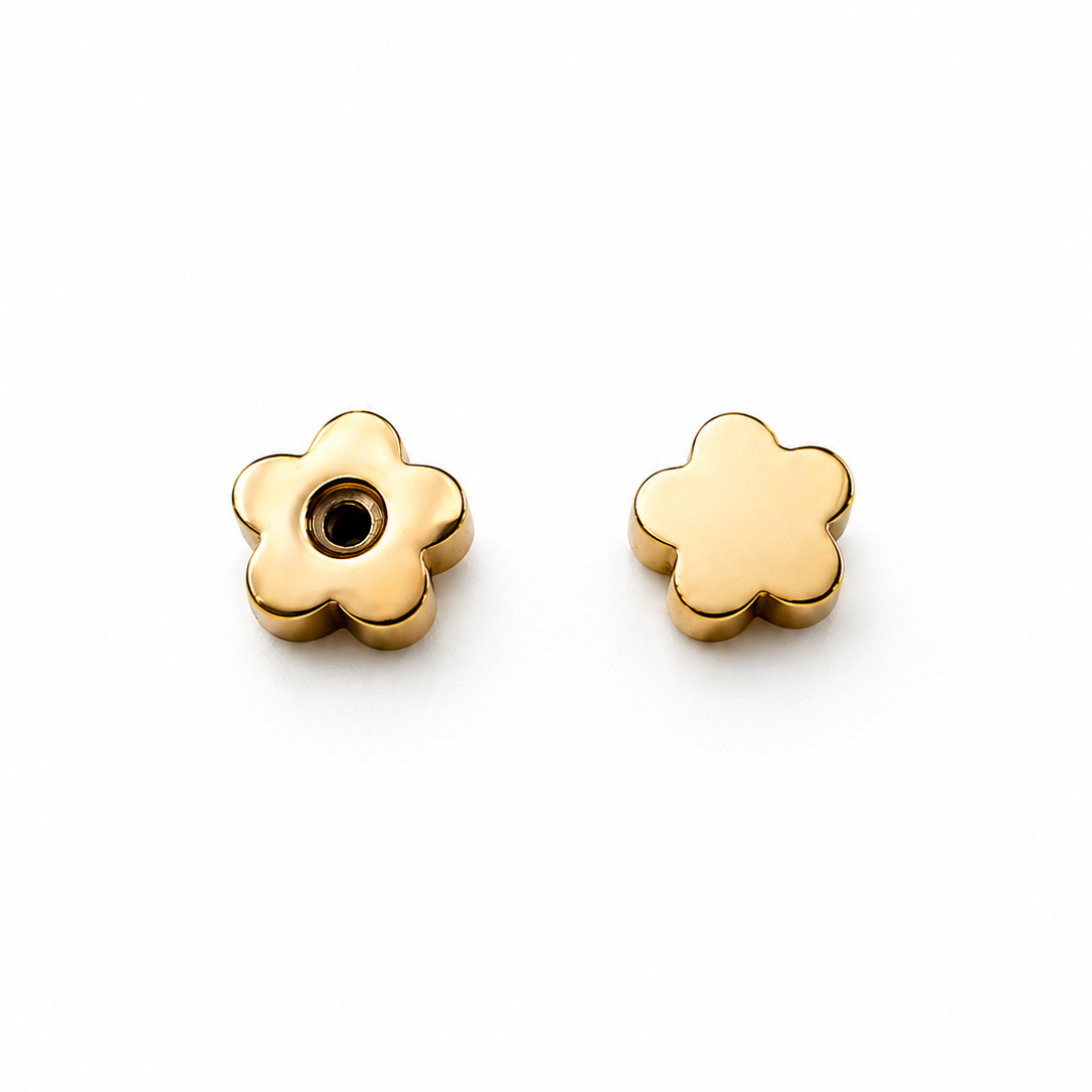 The JaxKelly Set of Flat Backs features two small, gold, flower-shaped charms made from 18K gold plated surgical grade stainless steel; one has a center hole, the other displays its solid back, shown on a white background.