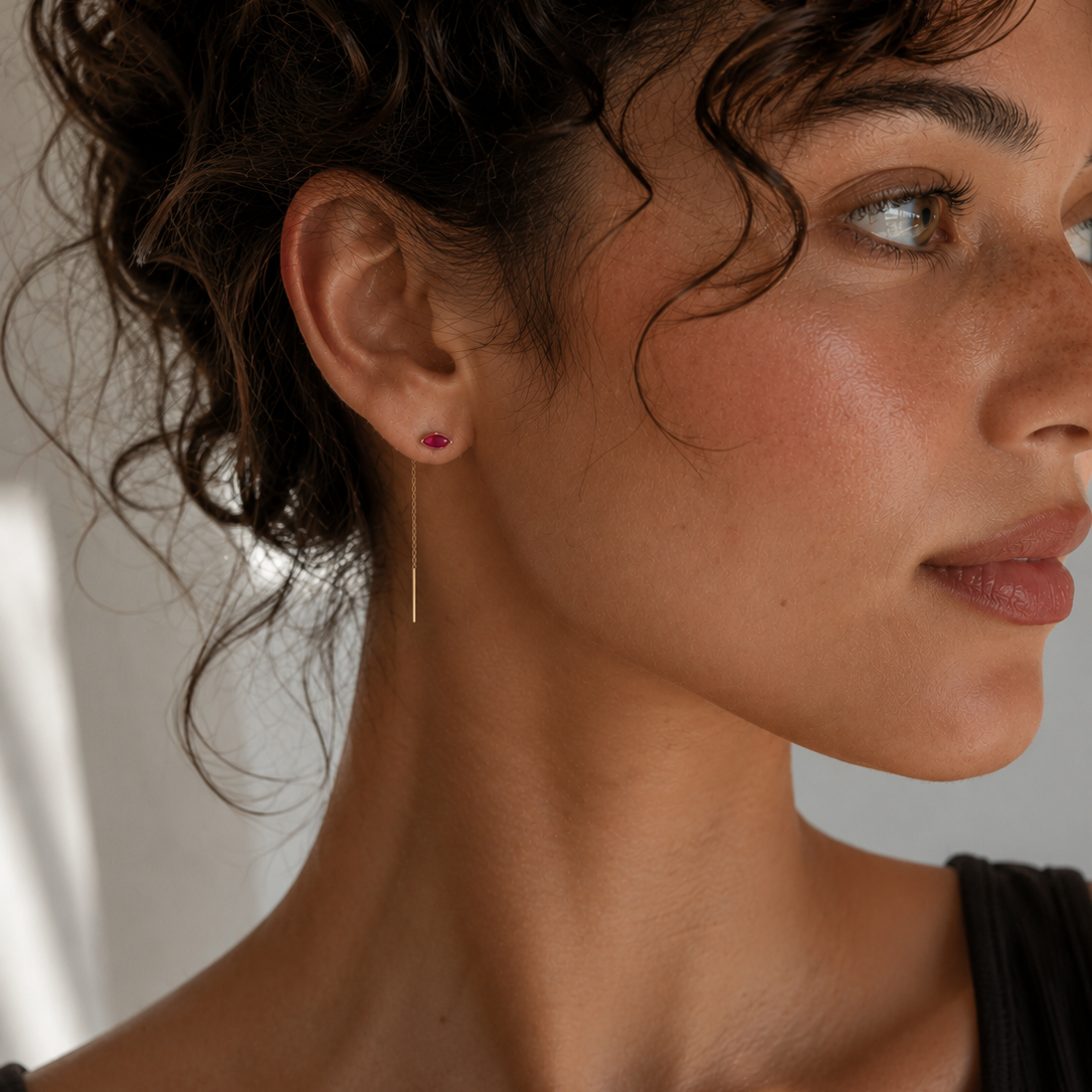 A woman with curly dark hair looks to the right, wearing JaxKelly’s Studded Threader - Pink CZ earring. Her skin glows naturally as soft sunlight highlights her face and neck above a simple black top.