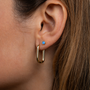Close-up of a woman's ear with two earrings: a JaxKelly Simple Stud Earring - Fire Opal in the upper lobe and a large, gold, elongated hoop below. The woman's light brown hair is partially visible.