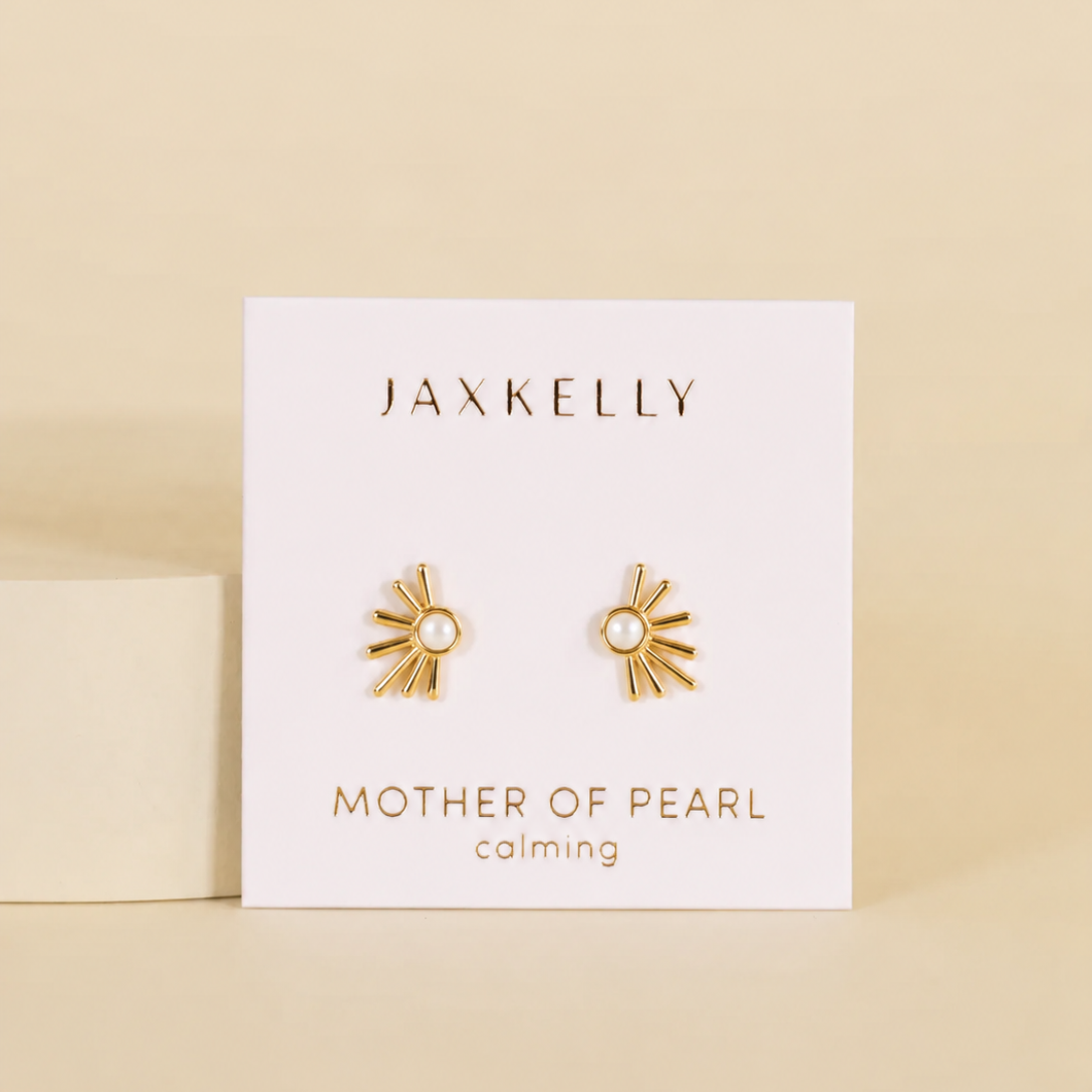 JaxKelly’s Sun Ray - Mother of Pearl stud earrings, featuring a pearl center, are displayed on a white card reading “Mother of Pearl” and “calming.” These elegant, hypoallergenic earrings combine gold sun ray design with gentle sophistication.