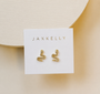The JaxKelly Pavé Snake earrings—gold plated and adorned with sparkling CZ stones—are displayed on a white JaxKelly card against a light beige background.