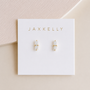 A pair of small, hypoallergenic 18K gold plated White Bar Druzy earrings by JaxKelly with clear natural druzy stone studs, displayed on a white JaxKelly card. Soft beige and cream tones in the background.