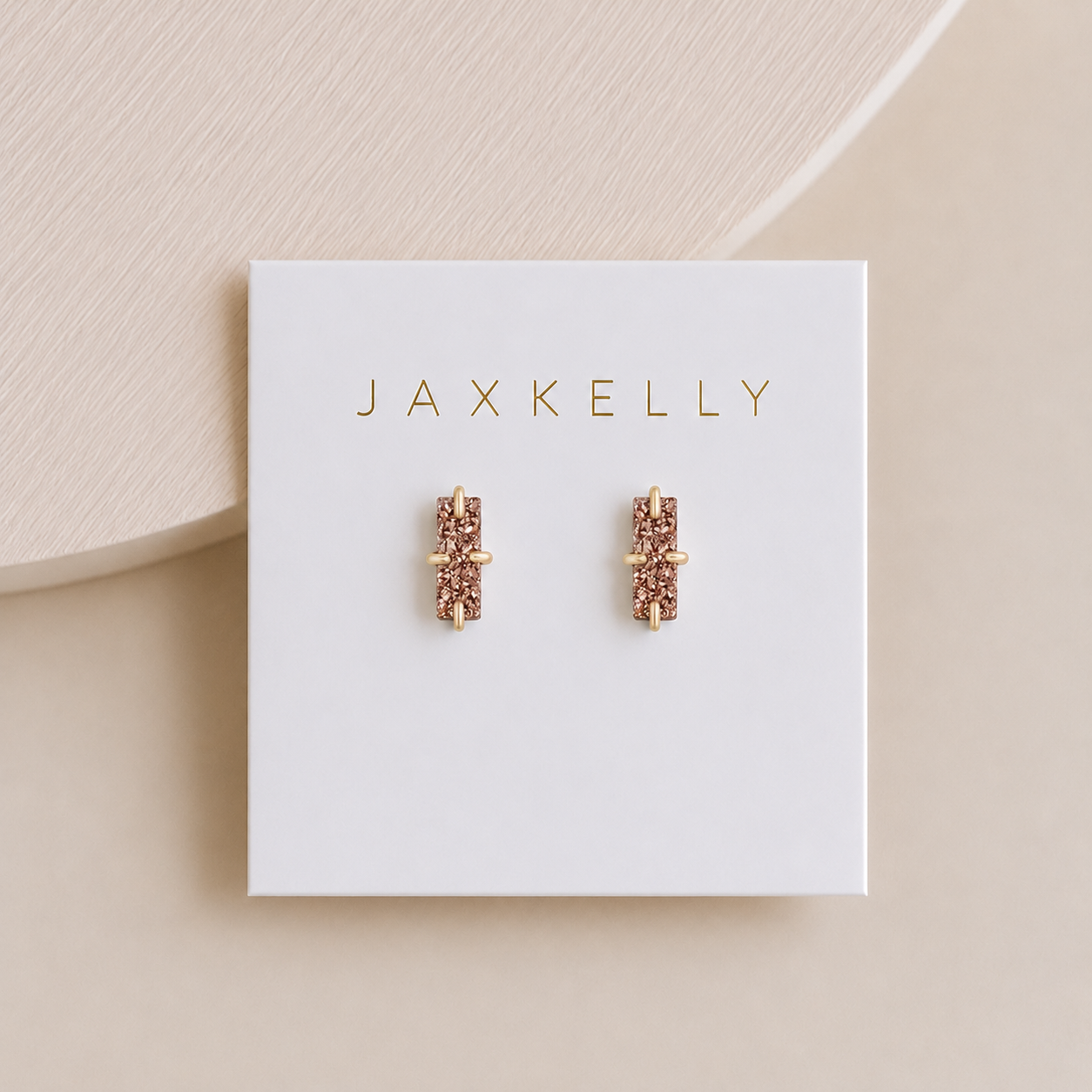 A pair of JaxKelly Rose Gold Bar Druzy stud earrings with pink gemstones, hypoallergenic and displayed on a white JaxKelly-branded card against a soft beige background.