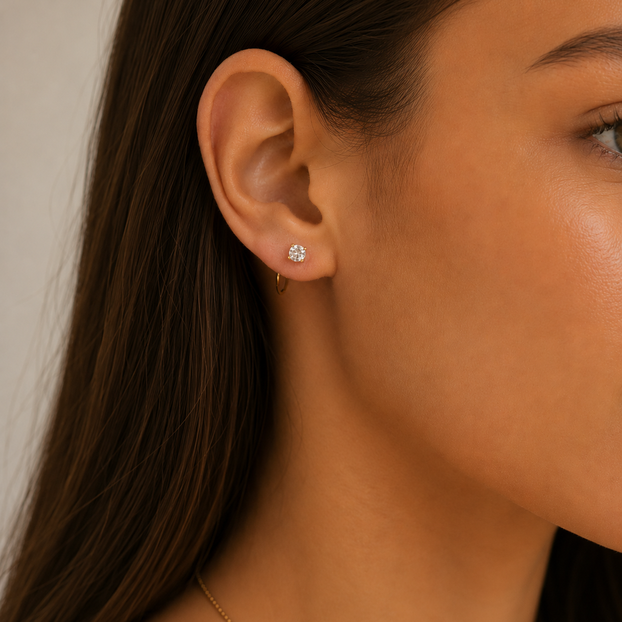 Close-up of a woman’s ear wearing the JaxKelly White CZ Huggie and a small diamond stud. Her sleek brown hair is tucked back, showing smooth skin and elegant, tarnish-free jewelry.