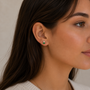 A woman with long brown hair, shown from the side against a neutral background, wears JaxKelly’s Double Stud Stack - Emerald CZ earring and a light beige top.