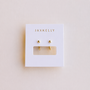 A pair of Gold Sphere Huggie earrings by JaxKelly displayed on a white, tarnish-free card with "JaxKelly" printed in gold at the top and a rectangular cutout beneath the earrings.