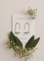 A pair of Amazonite Gemstone Drop - Hope earrings by JaxKelly, 18k gold plated, displayed on a white card reading "AMAZONITE hope," surrounded by green leaves and sprigs on a beige background.