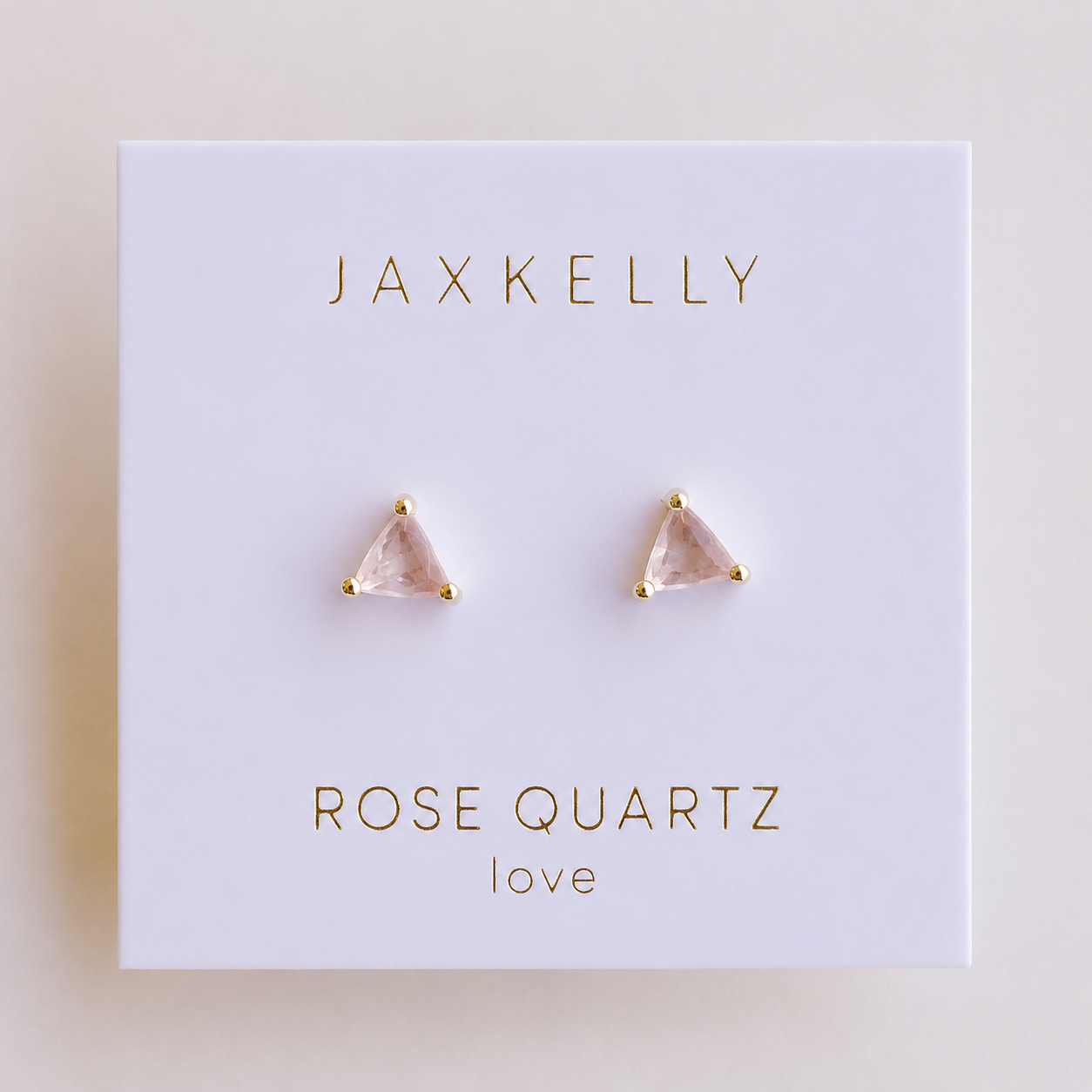 A pair of JaxKelly Rose Quartz Mini Energy Gems - Love studs with 18k gold plating and sterling silver posts, shown on a white card labeled JaxKelly and "Rose Quartz love" in gold lettering.