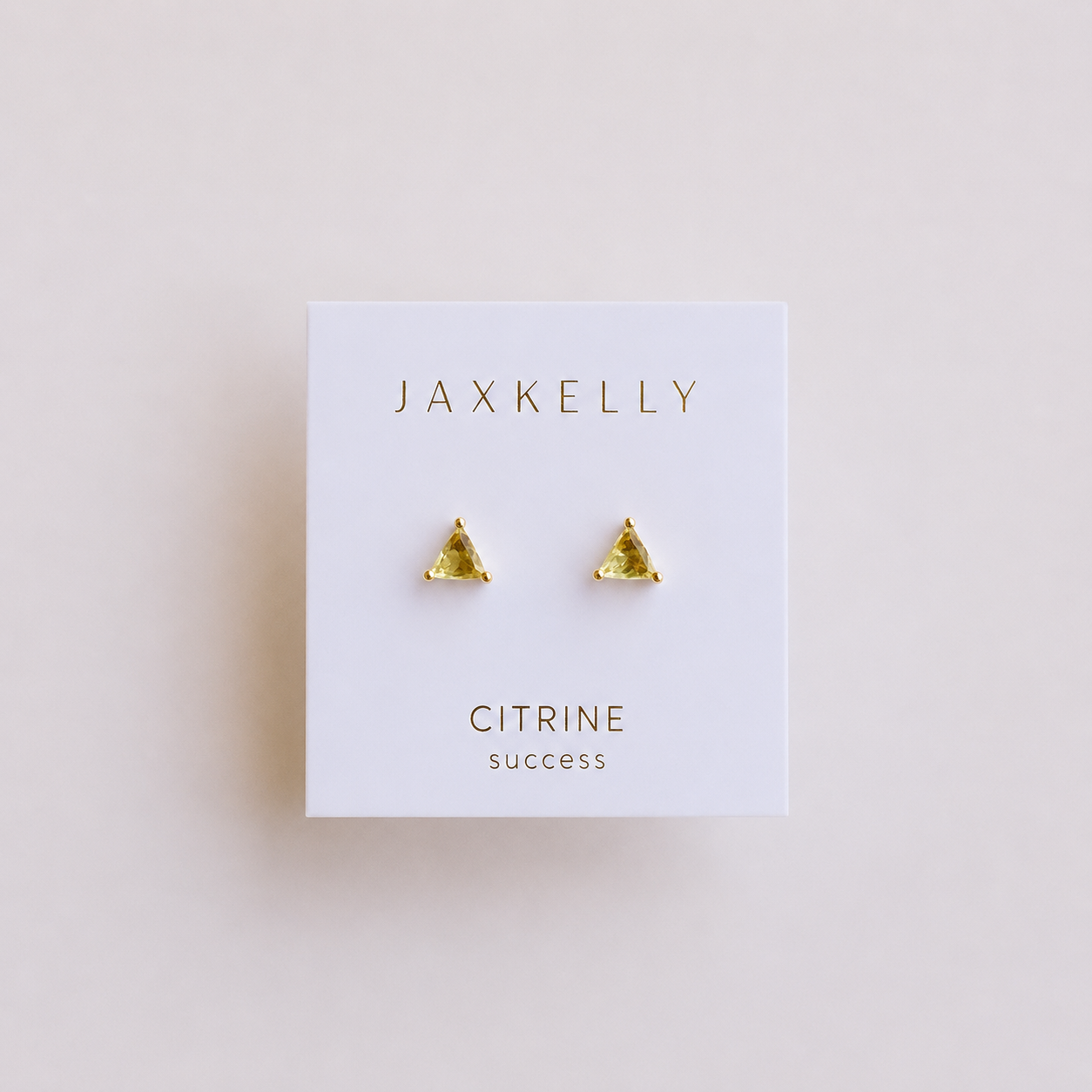 A pair of JaxKelly Citrine - Mini Energy Gems - Success studs with small, triangular yellow gemstones are displayed on a white JaxKelly card. These earrings feature 18k gold plating and sterling silver posts.