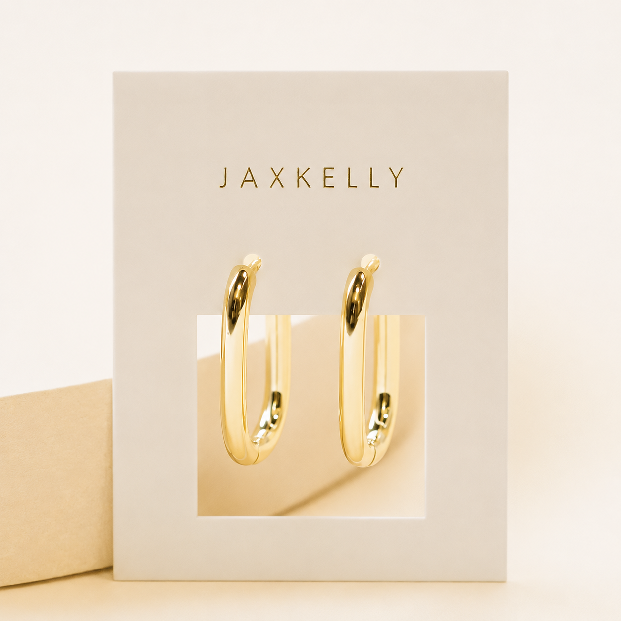 A pair of Large Rectangle Hoops by JaxKelly, featuring shiny, oversized rectangular hoops with 18k gold plating, displayed on a white card with “JaxKelly” printed in gold lettering at the top.