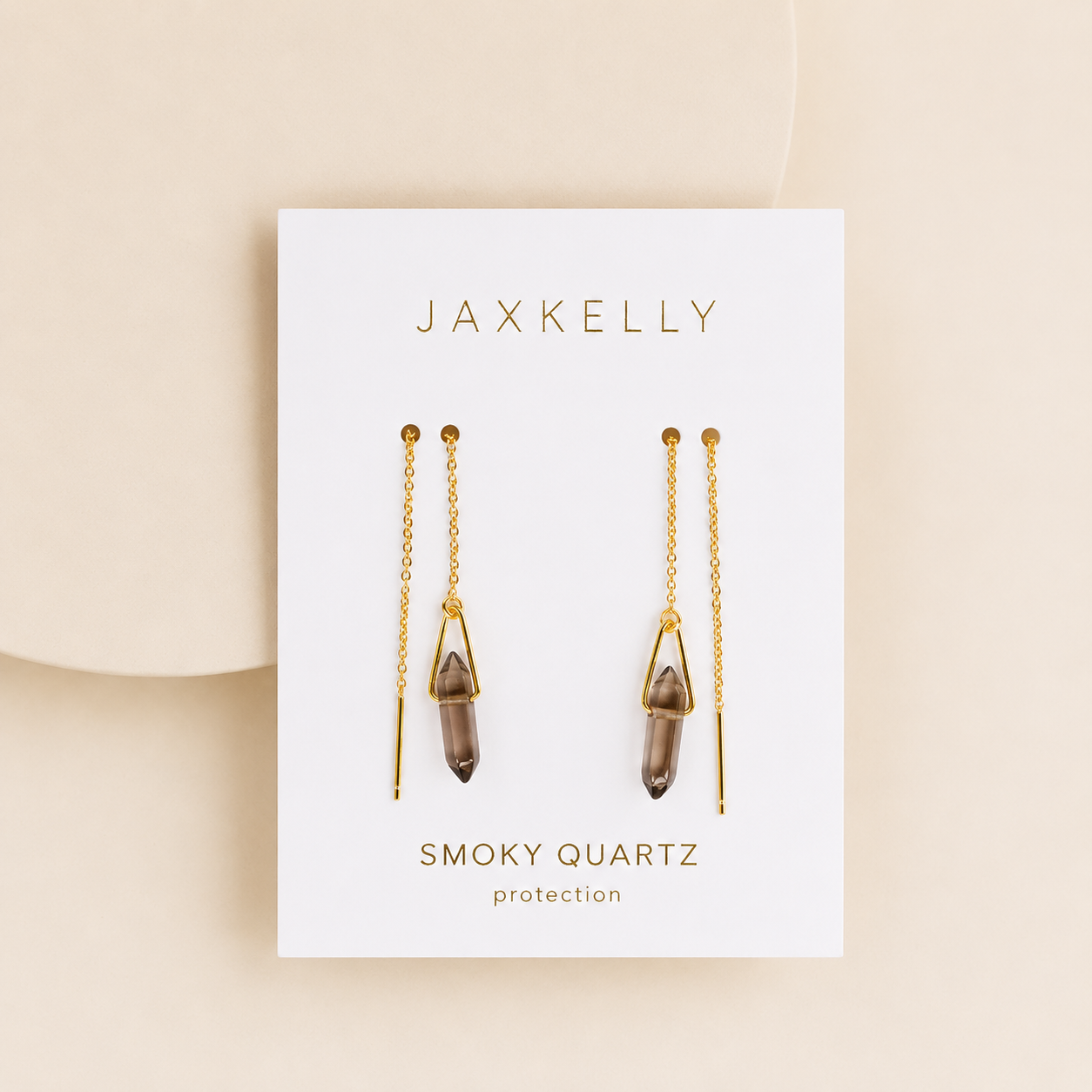 The Gemstone Threader - Smoky Quartz earrings by JaxKelly feature crystal pendants and are displayed on a white card with “Smoky Quartz protection” in gold, set against a beige background.