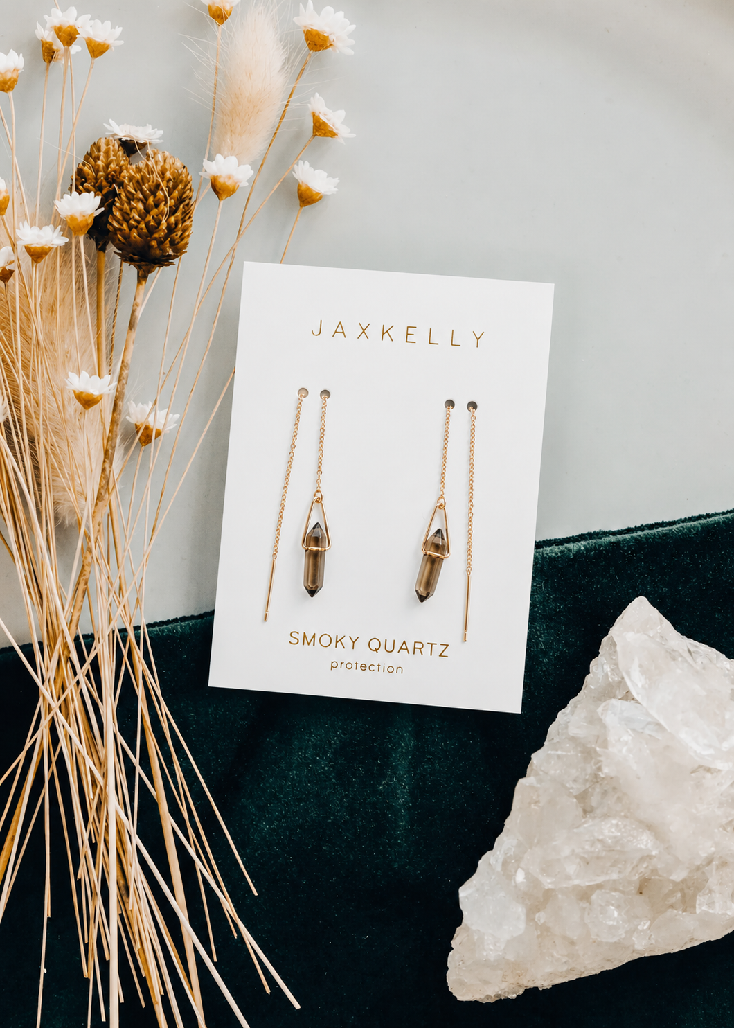 The Gemstone Threader - Smoky Quartz earrings by JaxKelly are shown on a branded card, accented with dried flowers and clear quartz crystal—an ideal minimalist accessory for any jewelry lover.