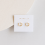 A pair of Minimalist Spiral gold-plated hoop earrings by JaxKelly, displayed on a white card with the brand name, set against a light neutral background.