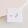 JaxKelly’s Star & Constellation earrings feature one large star on the left and a cascade of five smaller stars on the right, 18k gold plated and displayed on a white card.