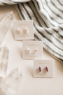 A JaxKelly Clear Quartz Mineral Point for cleansing is displayed on a light surface with crystals and striped fabric in the background.