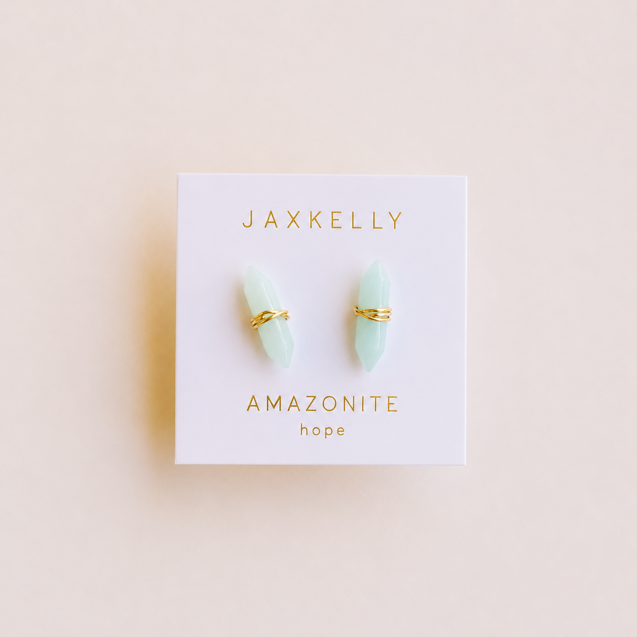 A pair of light green amazonite mineral point earrings, wrapped in 18k gold by JaxKelly, shown on a white card labeled "JaxKelly Amazonite Mineral Point - Hope" in gold text, set against a light beige background.