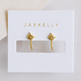 The JaxKelly Star Huggie earrings feature an 18K gold-plated starburst design with a clear center stone, displayed on a white card with "JAXKELLY" in gold letters.