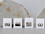 Four pairs of JaxKelly earrings, including Pavé Silver Hoop styles, are displayed on branded cards before two large rocks on a light gray background. The cards feature unique rhodium-plated designs from hoops to detailed studs.