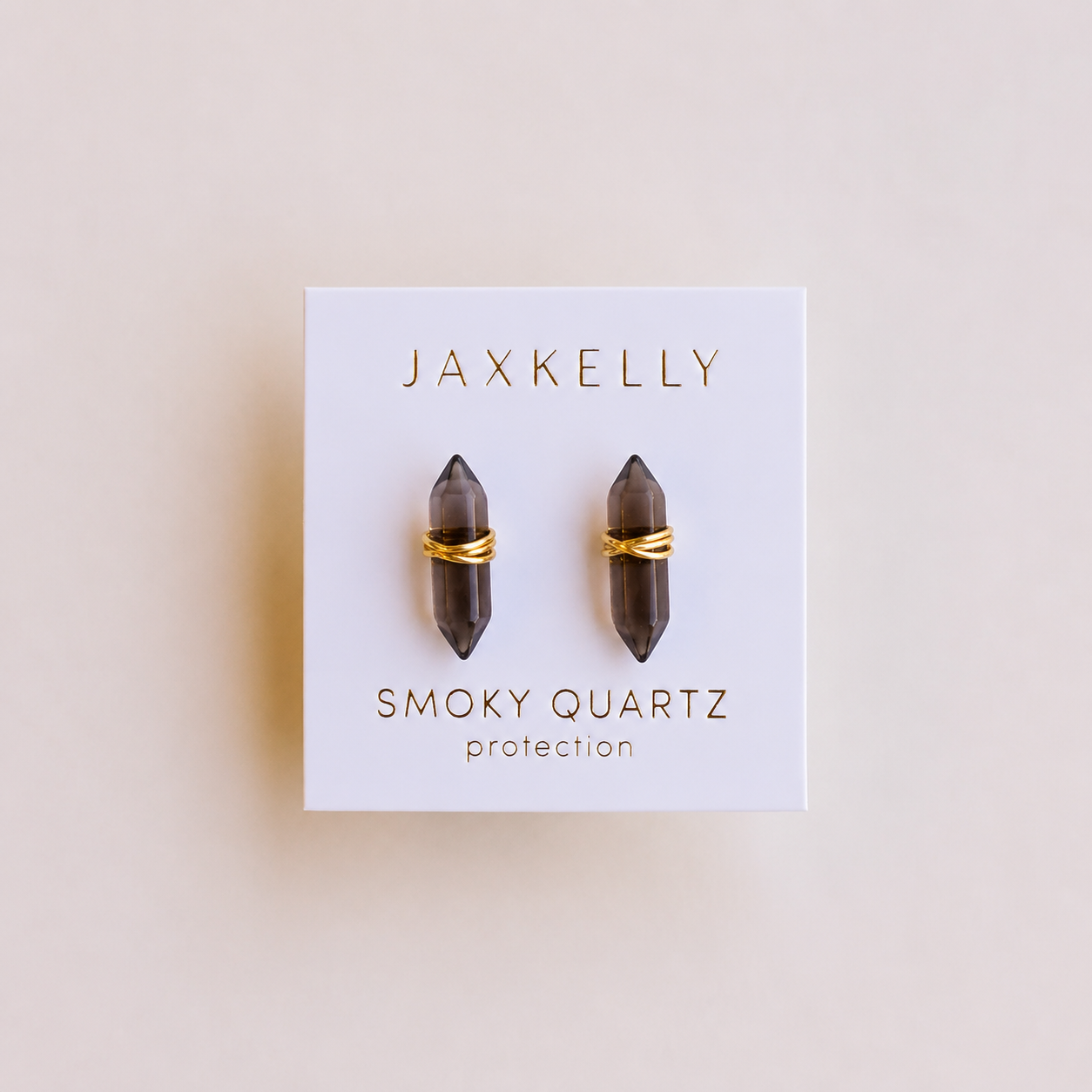 A pair of smoky quartz mineral point earrings by JaxKelly, labeled "Smoky Quartz Mineral Point - Protection," are displayed on a white card with gold and gray lettering.