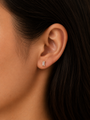 Close-up of a woman's ear with straight dark hair, wearing JaxKelly's Clear Baguette stud earring. This small, hypoallergenic design offers a stylish and comfortable look with its minimalist clear baguette detailing.
