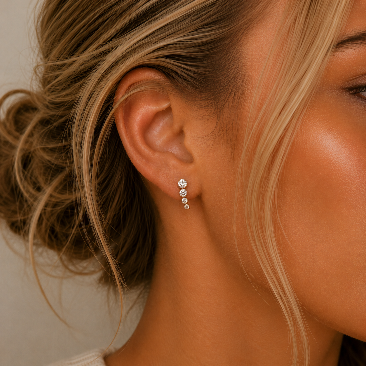 Close-up of a woman's ear wearing JaxKelly's Mini Crawler Gold Earrings with dazzling white CZ stones. Her blonde hair is styled in a loose bun, and the lighting highlights her glowing skin and the sparkling jewelry.