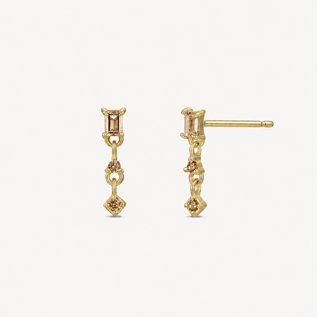 The JaxKelly Mini Baguette Drop - Champagne CZ earrings showcase a rectangular champagne stone with round and diamond-shaped accents. These tarnish-free gold drop earrings are displayed on a plain white background.