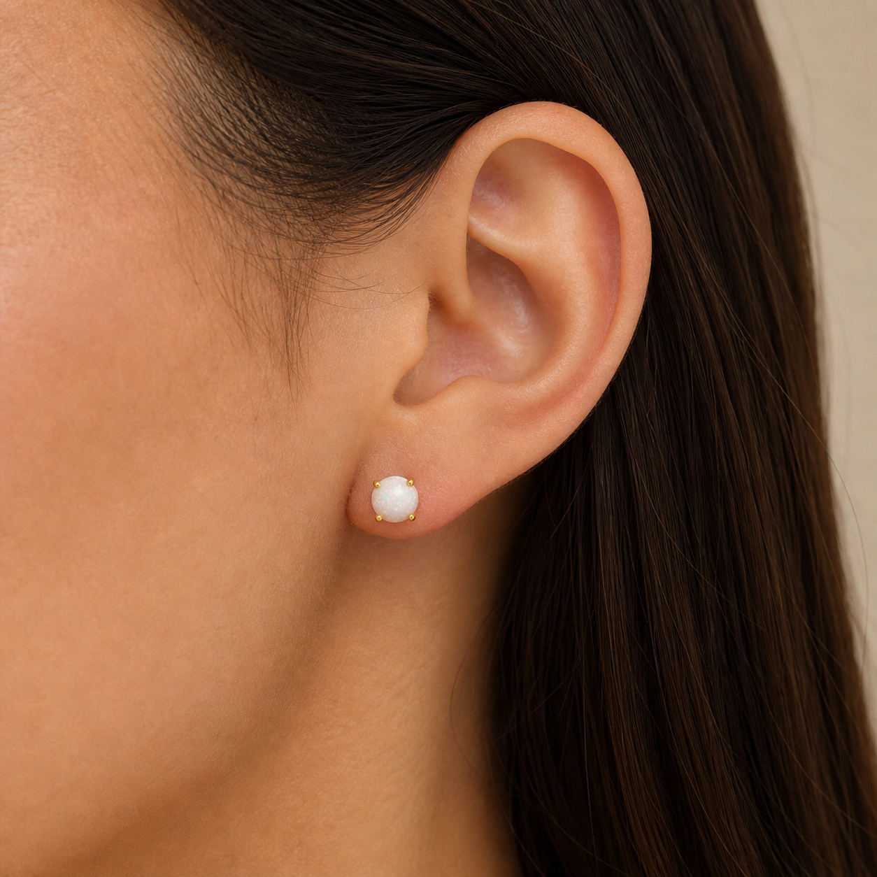 Close-up of a woman with straight brown hair wearing JaxKelly's Round - White Opal Gemstone - Gold Earrings.