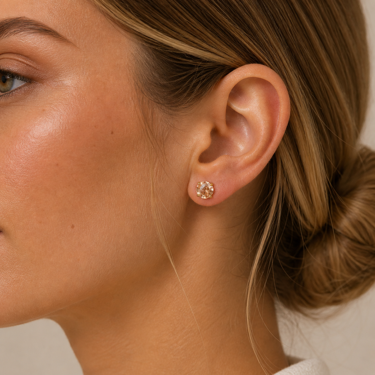 Close-up of a woman wearing JaxKelly's Round CZ- Champagne - Gold Earrings. Her light brown hair is in a low bun, and she has clear skin with natural makeup for a minimalist look.