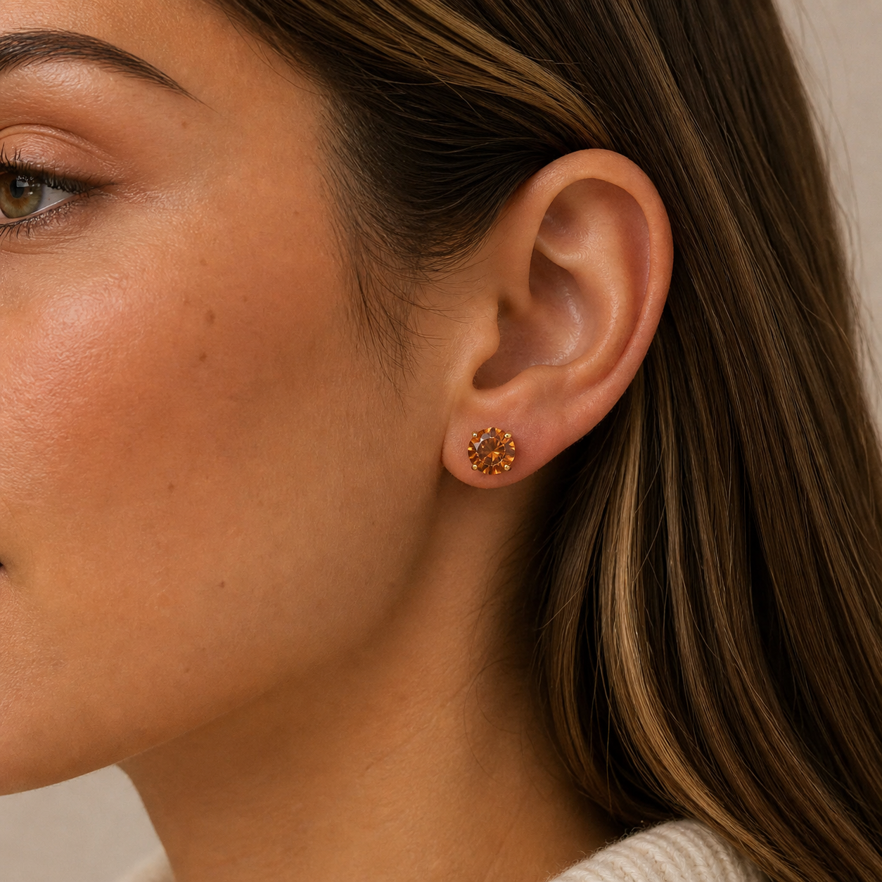 Close-up of a woman with light skin and straight brown hair wearing JaxKelly's Round CZ - Coffee - Gold Earrings—gold-plated studs in a sunburst design.