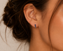 A close-up shows a woman’s ear wearing JaxKelly’s Mini Crawler - Sapphire CZ - Gold Earrings; her loose bun highlights the elegant vertical row design against her warm, natural-toned skin.