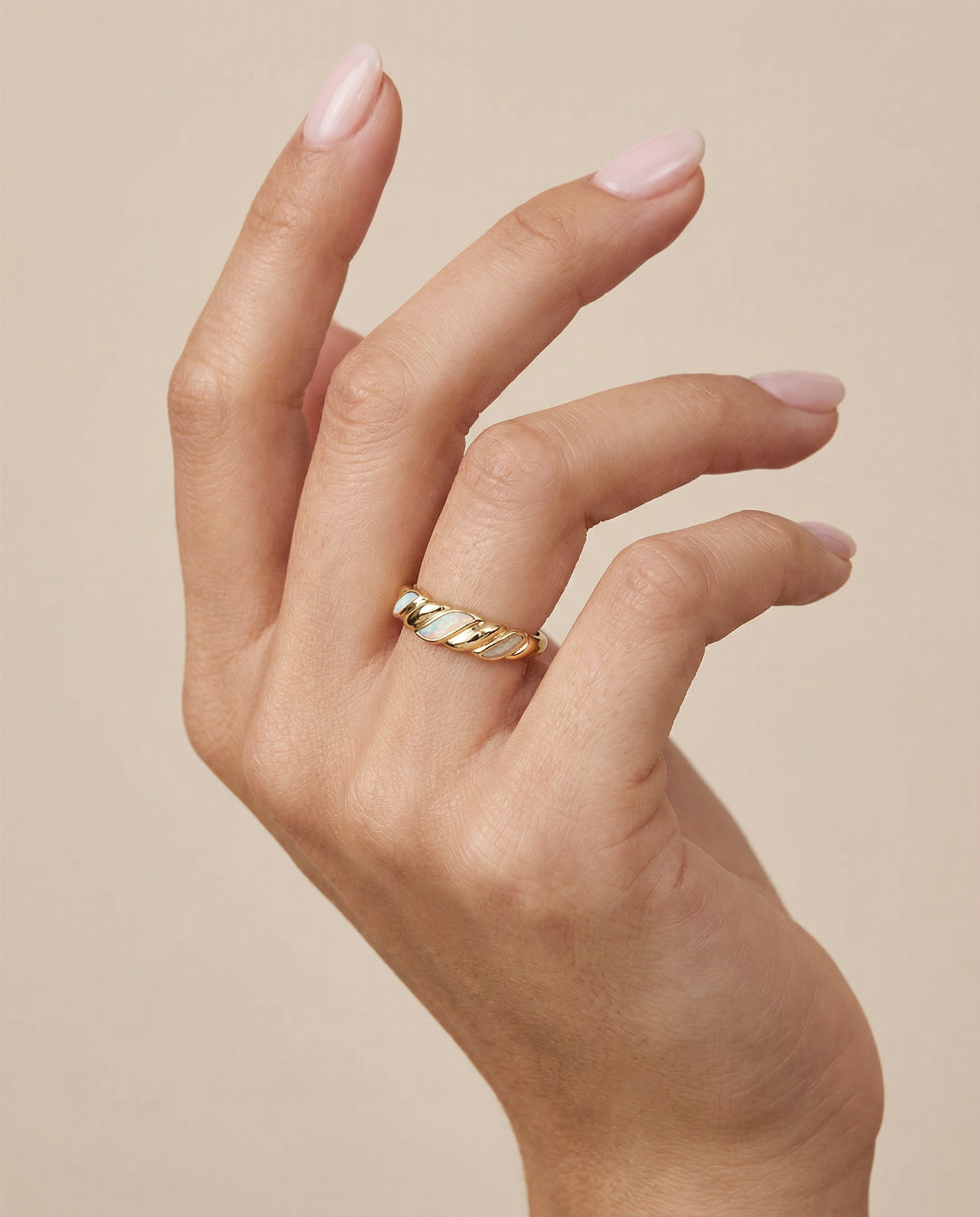 A manicured hand with pale pink nails displays the Gold Twist Ring - White Opal, featuring a thick gold band and twisted design, against a neutral background.