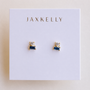 The JaxKelly Sapphire Double Stack earrings feature rectangular sapphire stones stacked with small CZs above, set in 18k gold plating. Displayed on a white card topped with gold JaxKelly branding.