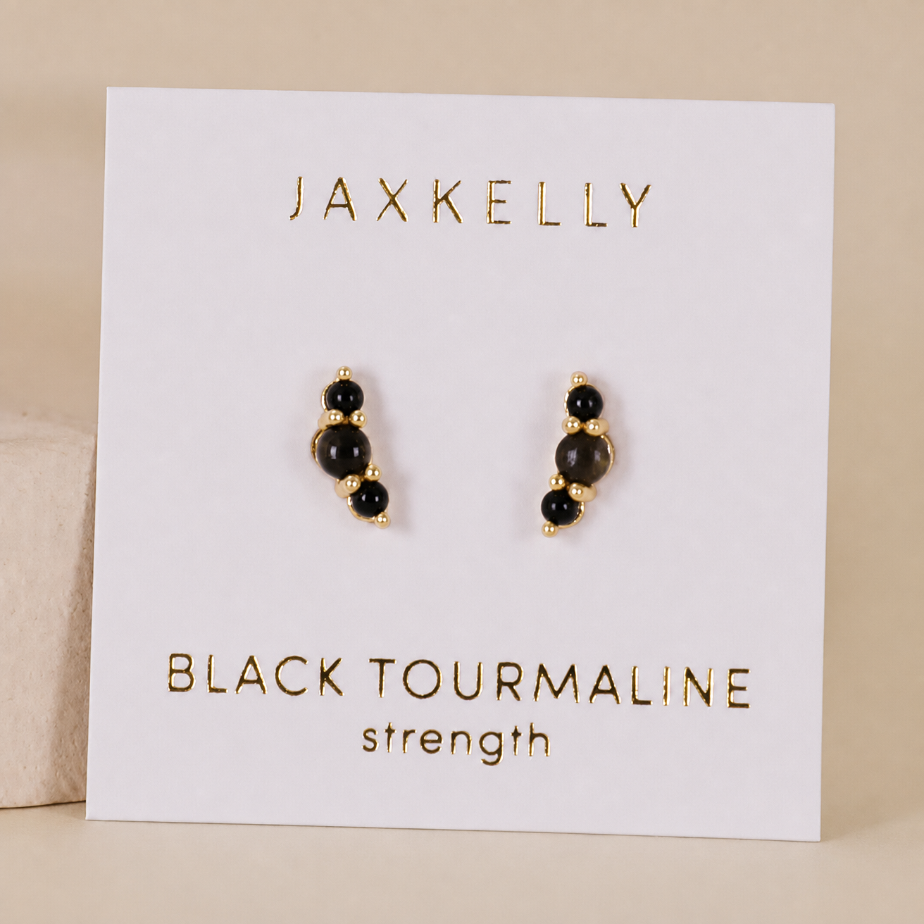 JaxKelly Crescent Gold Earrings – Black Tourmaline feature gold-plated studs with sterling silver posts, displayed on a white card with “JaxKelly Crescent Gold Earrings - Black Tourmaline” in gold lettering.