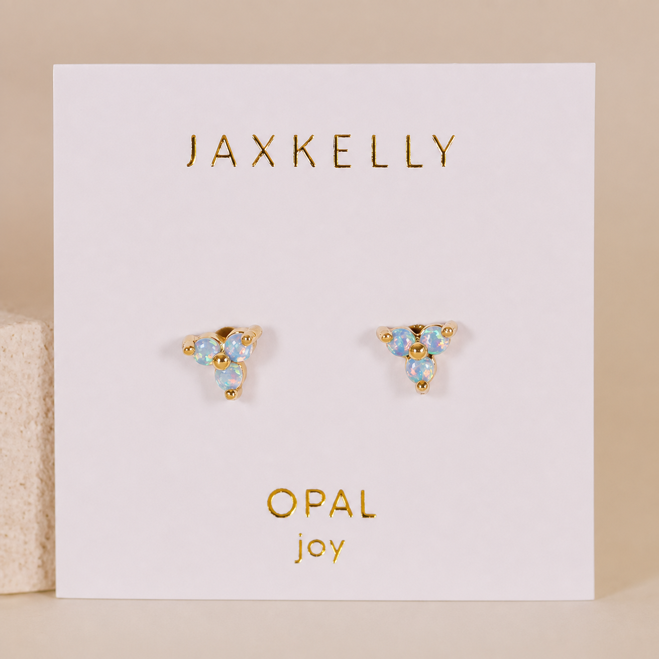 The Trio Cluster Gold Earrings - Fire Opal by JaxKelly feature three lab-grown fire opals on gold-plated settings, displayed on a white card labeled JAXKELLY at the top and OPAL joy in gold at the bottom.