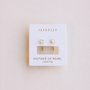 The JaxKelly Mother of Pearl Huggie earrings, featuring a minimalist gold and pearl design, are displayed on a white card labeled “calming” against a light background.