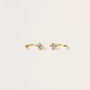 A pair of Mystery Earrings—delicate gold open hoops, each with a small round clear gemstone at the center—displayed on a plain light background.