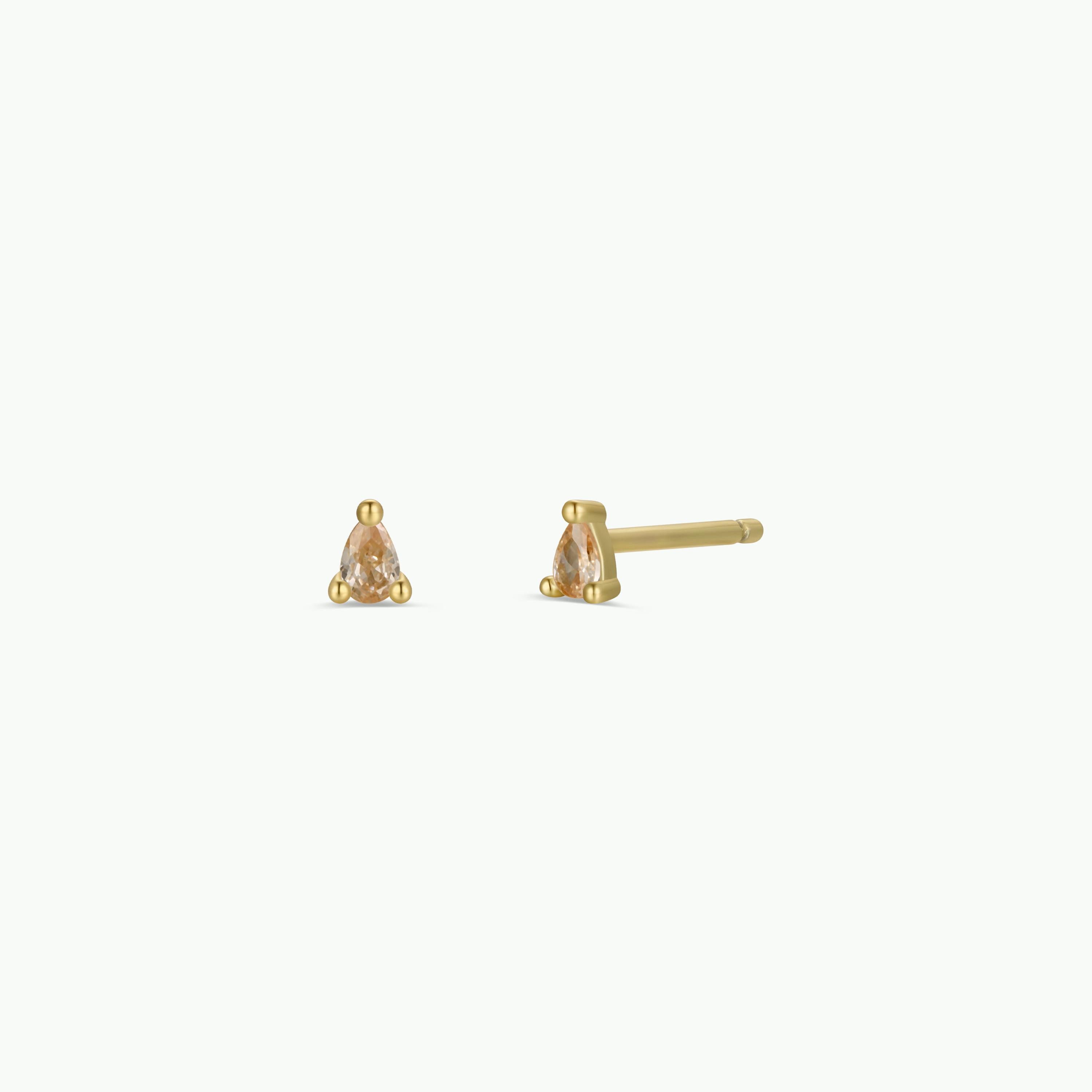 The Teardrop Stud - Champagne CZ earrings feature 18k gold-plated studs and sterling silver posts, each with a small, clear champagne cubic zirconia in a triangular setting, displayed from front and side on a white background.