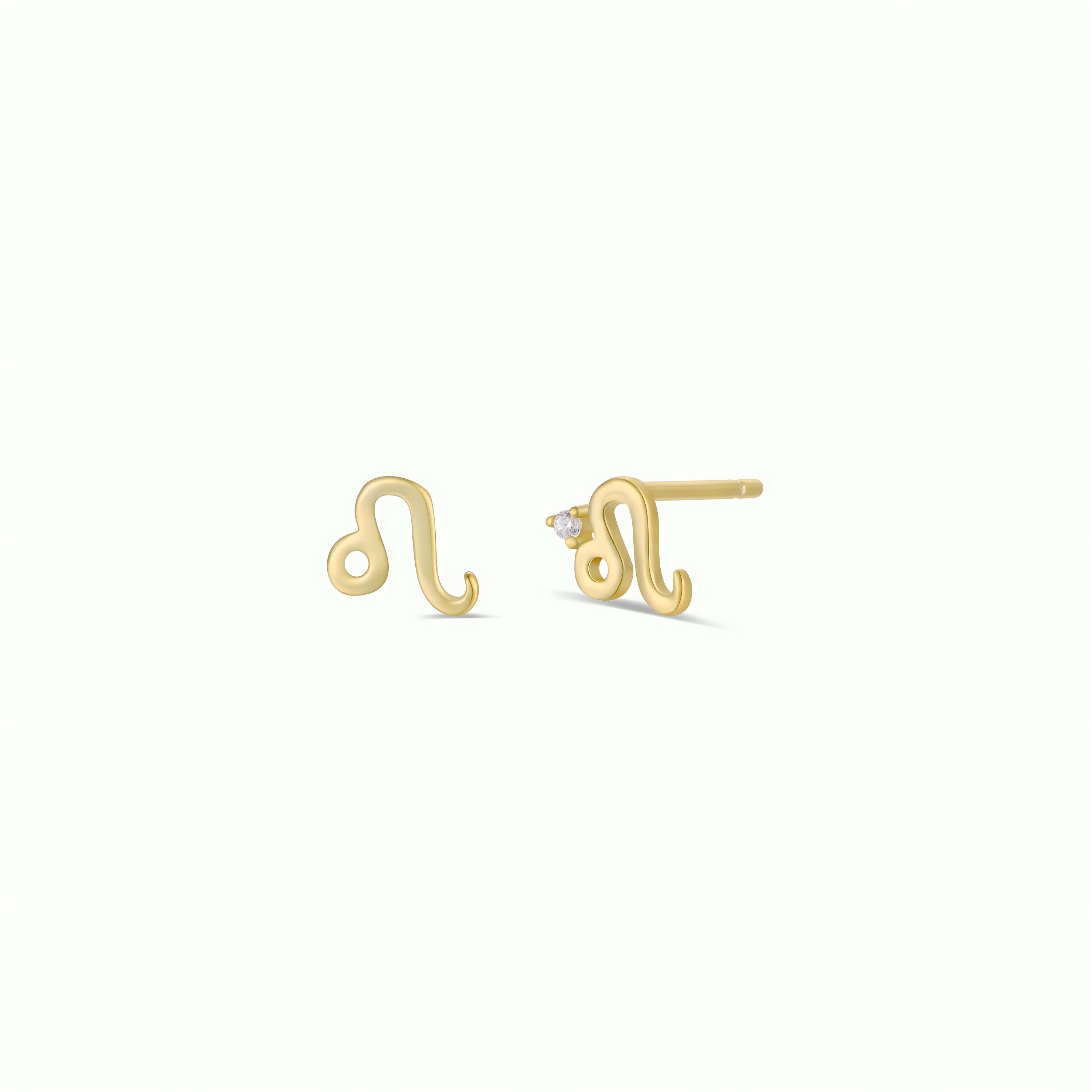 Zodiac Earrings - Leo: A pair of 18k gold plated stud earrings shaped like the Leo zodiac sign, with one earring featuring a small gemstone. Shown on a plain, light-colored background.