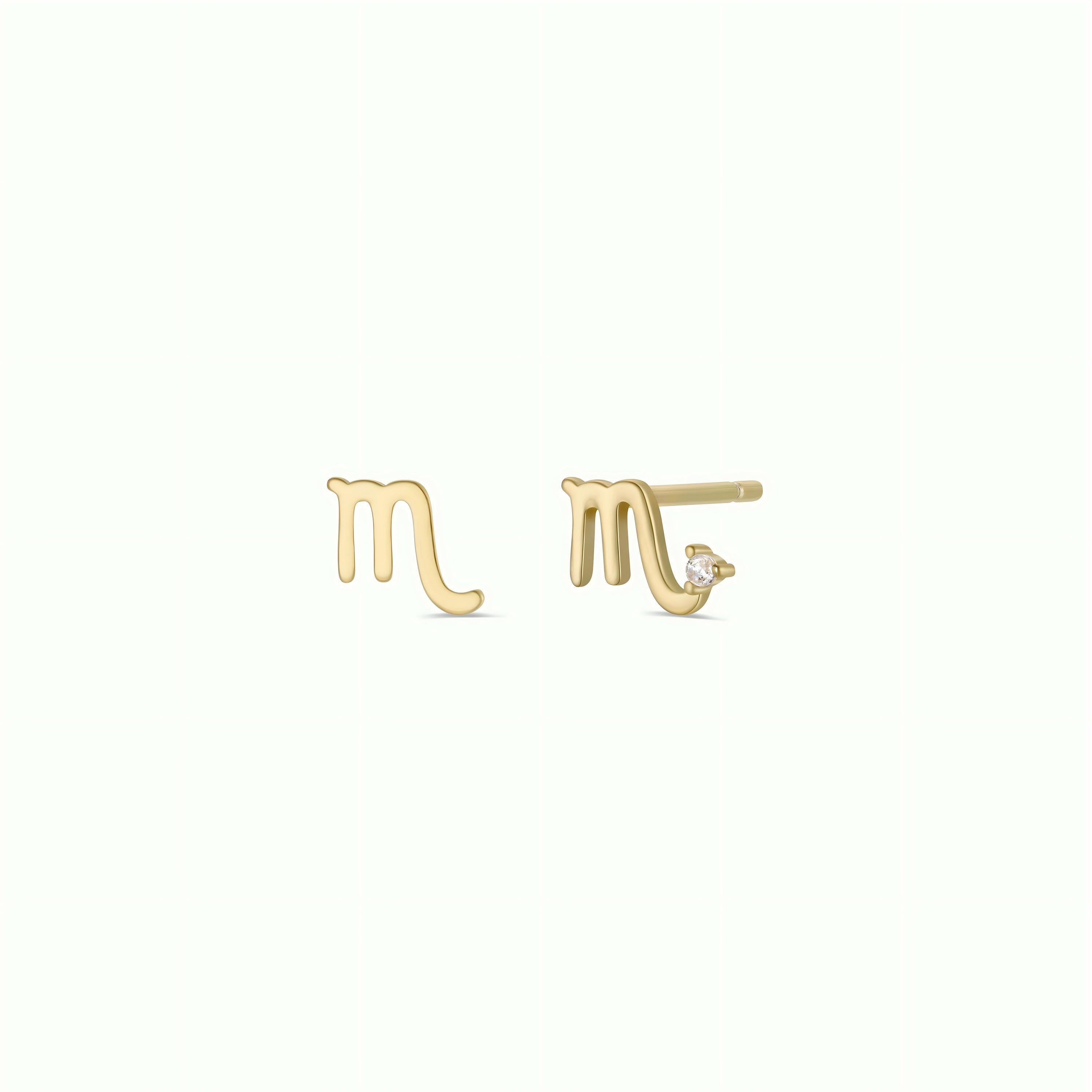 A pair of 18k Gold Plated Virgo Zodiac Earrings, one featuring a small clear gemstone accent. These charm studs are set against a plain, light-colored background.