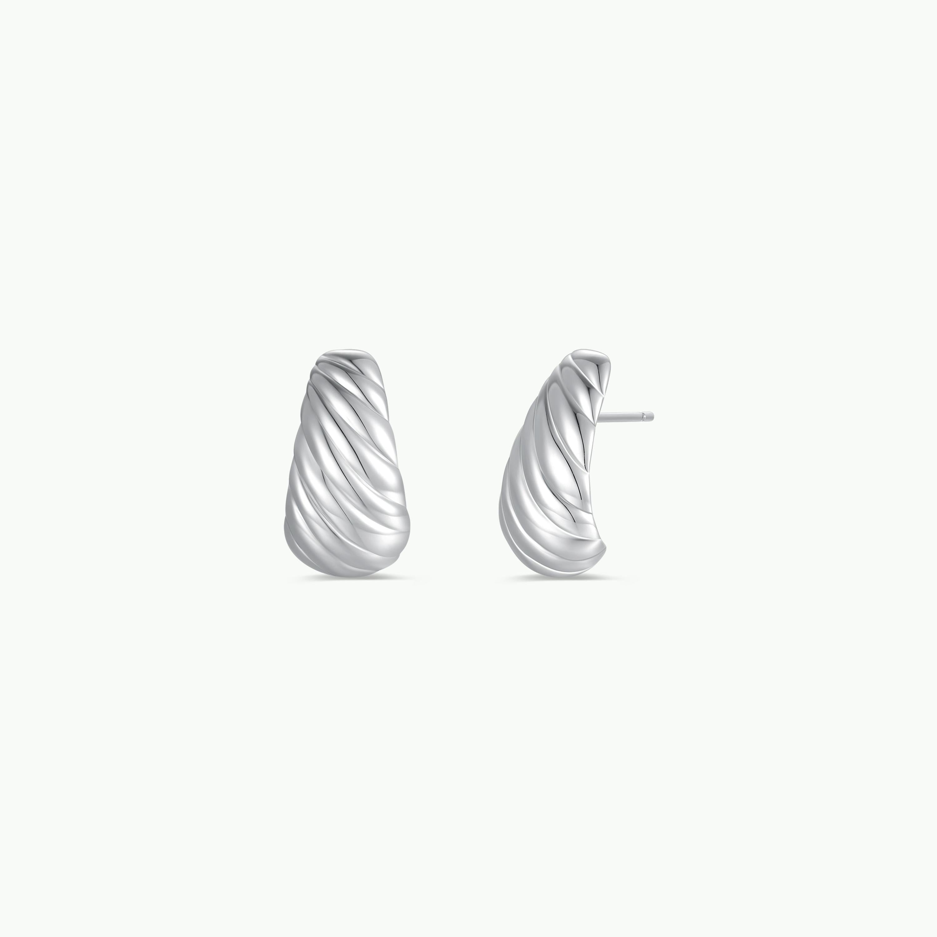The Silver Bold Swirl - Earring features a ribbed, twisted sterling silver design. Shown from the front and side, these curved earrings have a textured finish with stud-style backs, giving a modern hoop-inspired look.
