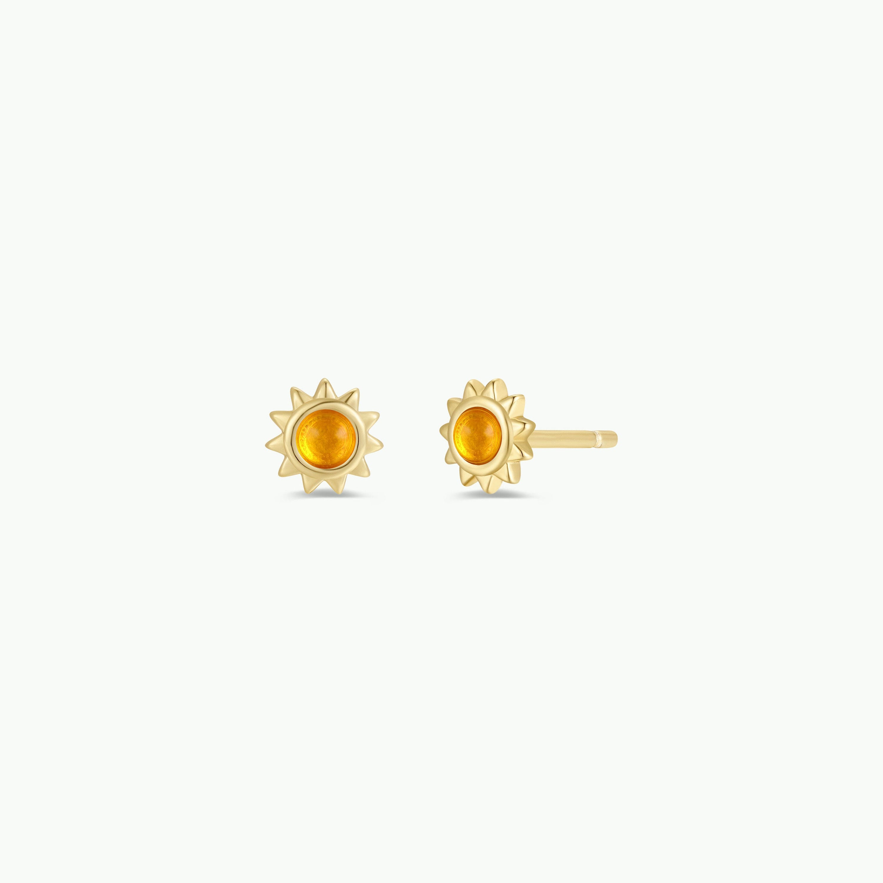 The Amber Sun Stud earrings feature a gold sun design with a round amber stone center and radiating rays, shown on a plain white background.