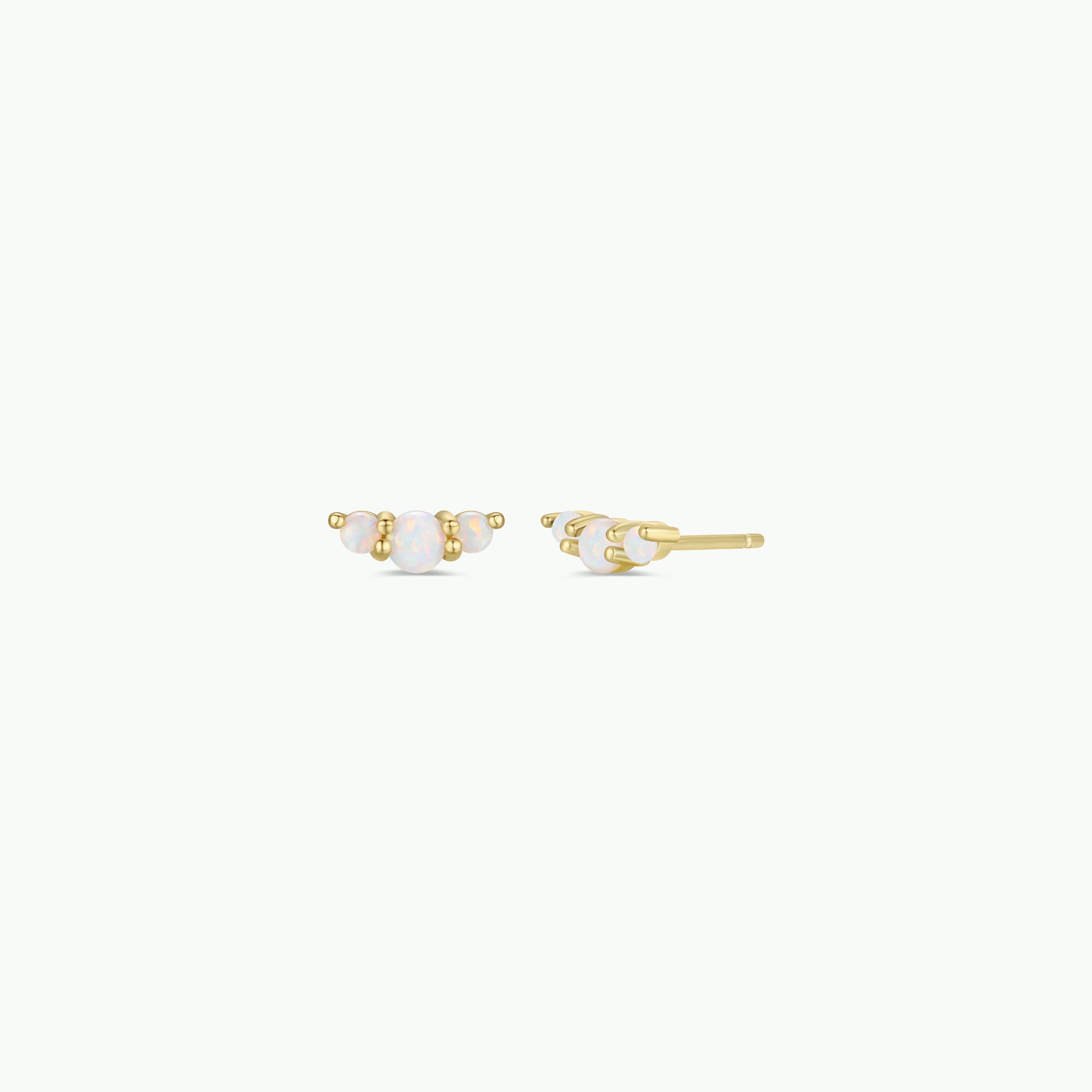 The Crescent Gold Earrings - White Opal are small gold-plated studs, each with three oval lab-grown opals in a row and gold prong settings, shown on a plain white background.