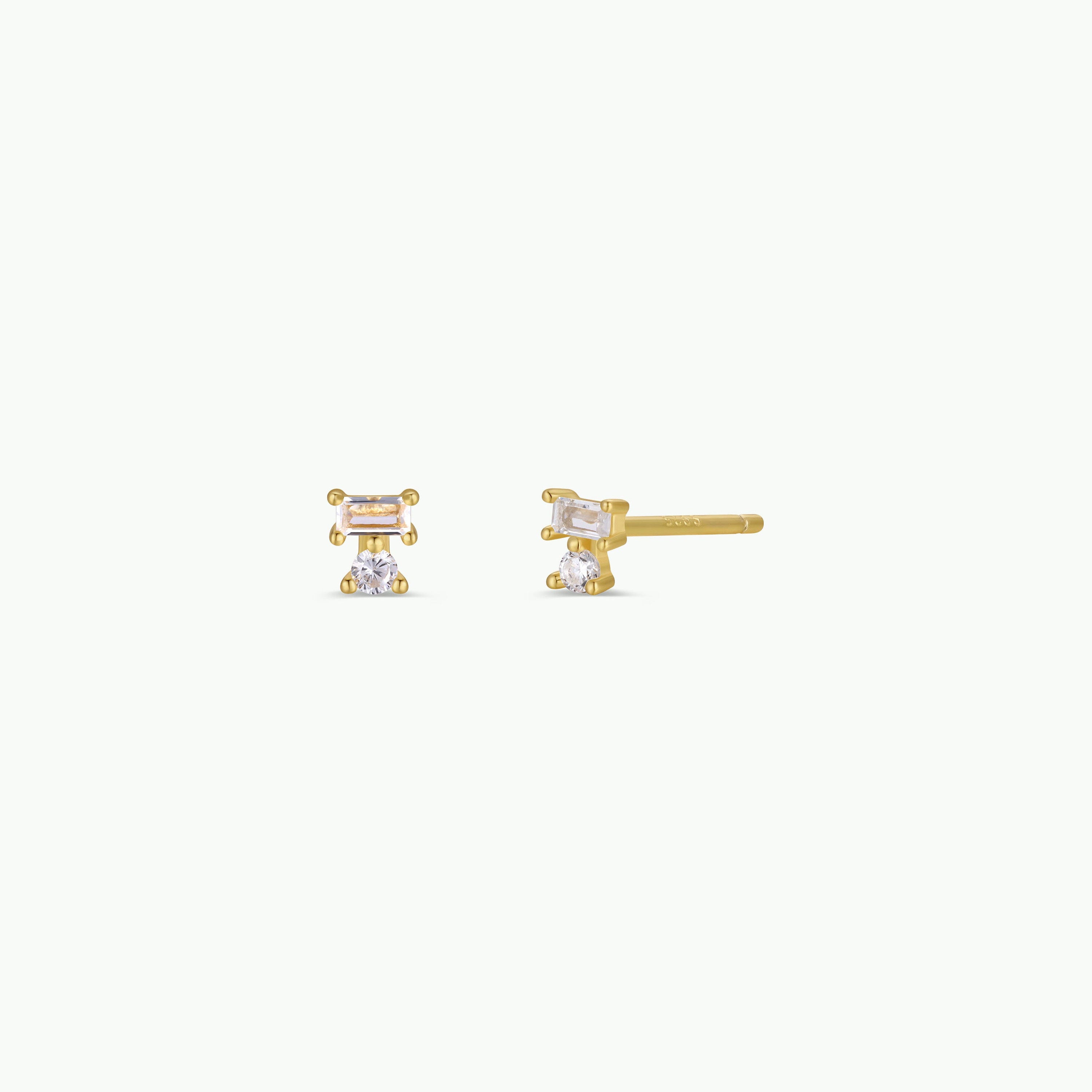 Double Stud Stack: Small gold stud earrings with two vertically arranged clear gemstones—a white baguette CZ stacked over another—set in a minimalist 18k gold-plated design.
